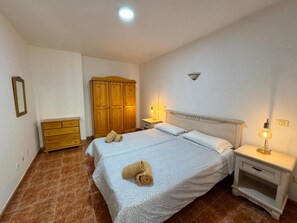 Une chambre à coucher avec un lit double, une armoire en bois, une table de chevet avec une lampe et une petite commode.