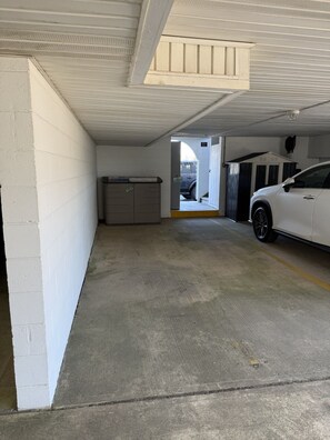 Un garaje de estacionamiento con un coche blanco aparcado en un espacio, paredes de hormigón y un techo metálico.
