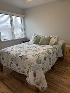 Un dormitorio con una cama, una mesita de noche, un aparador de madera y una ventana con persianas.
