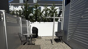 Eine Terrasse mit Tisch, Stühlen, einem Grill und einem weißen Zaun.