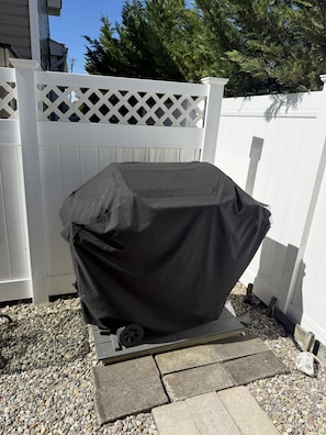A covered grill in a backyard with a white fence and a stone pathway. - Ocean Block- Renovated 2 Bedroom 1 Bath Condo (Seaside Park)