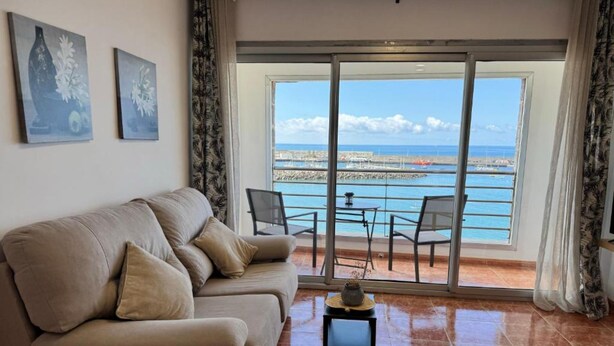 Una sala de estar con sofá, una mesita y vista al mar a través de un ventanal.