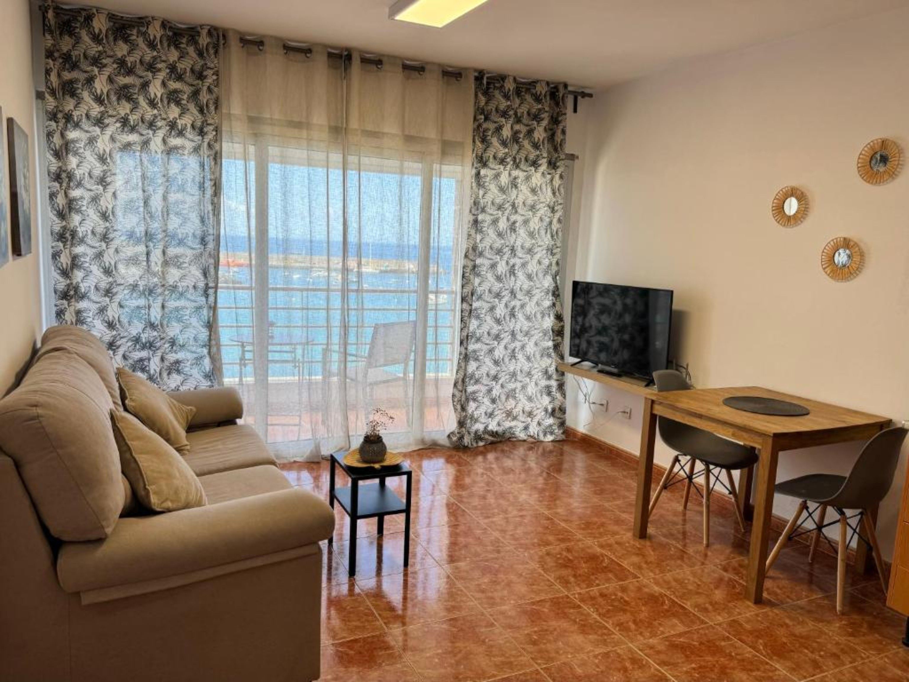 Una sala de estar con un sofá, una mesita, un televisor y un comedor con sillas.