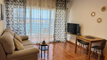 Una sala de estar con un sofá, una mesita, un televisor y un comedor con sillas.