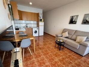 Ett kompakt bostadsutrymme med ett litet kök, en matplats och en sittgrupp med en soffa och ett litet sidobord.