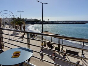 Un paseo marítimo con barandilla, mesas y gente caminando.