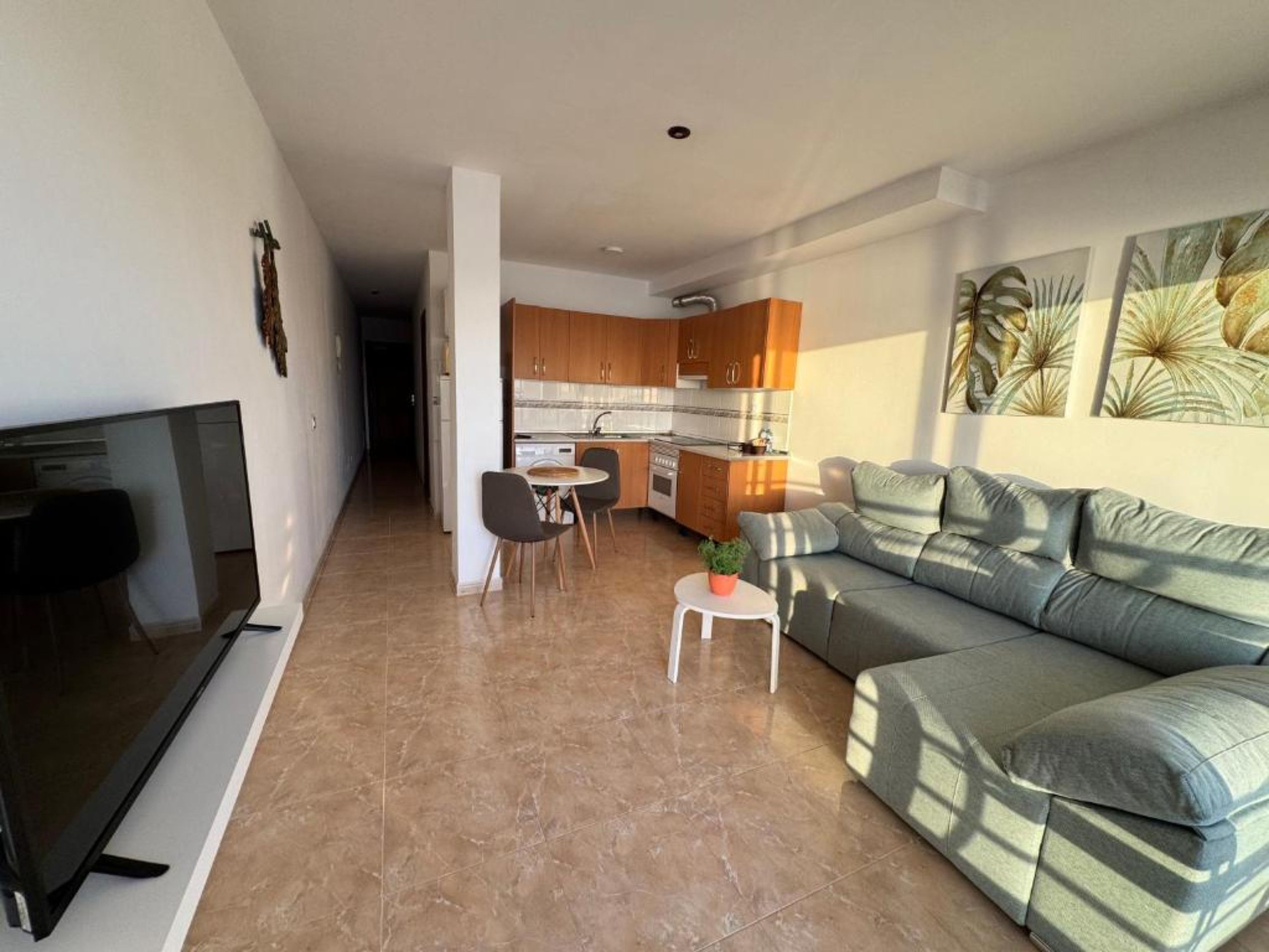 A modern living room with a sofa, a TV, and a dining area with chairs and a table.
