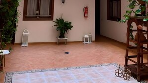 A spacious indoor courtyard with a tiled floor, potted plants, and a wooden structure.