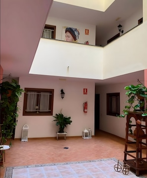A spacious indoor courtyard with a tiled floor, potted plants, and a wooden structure.