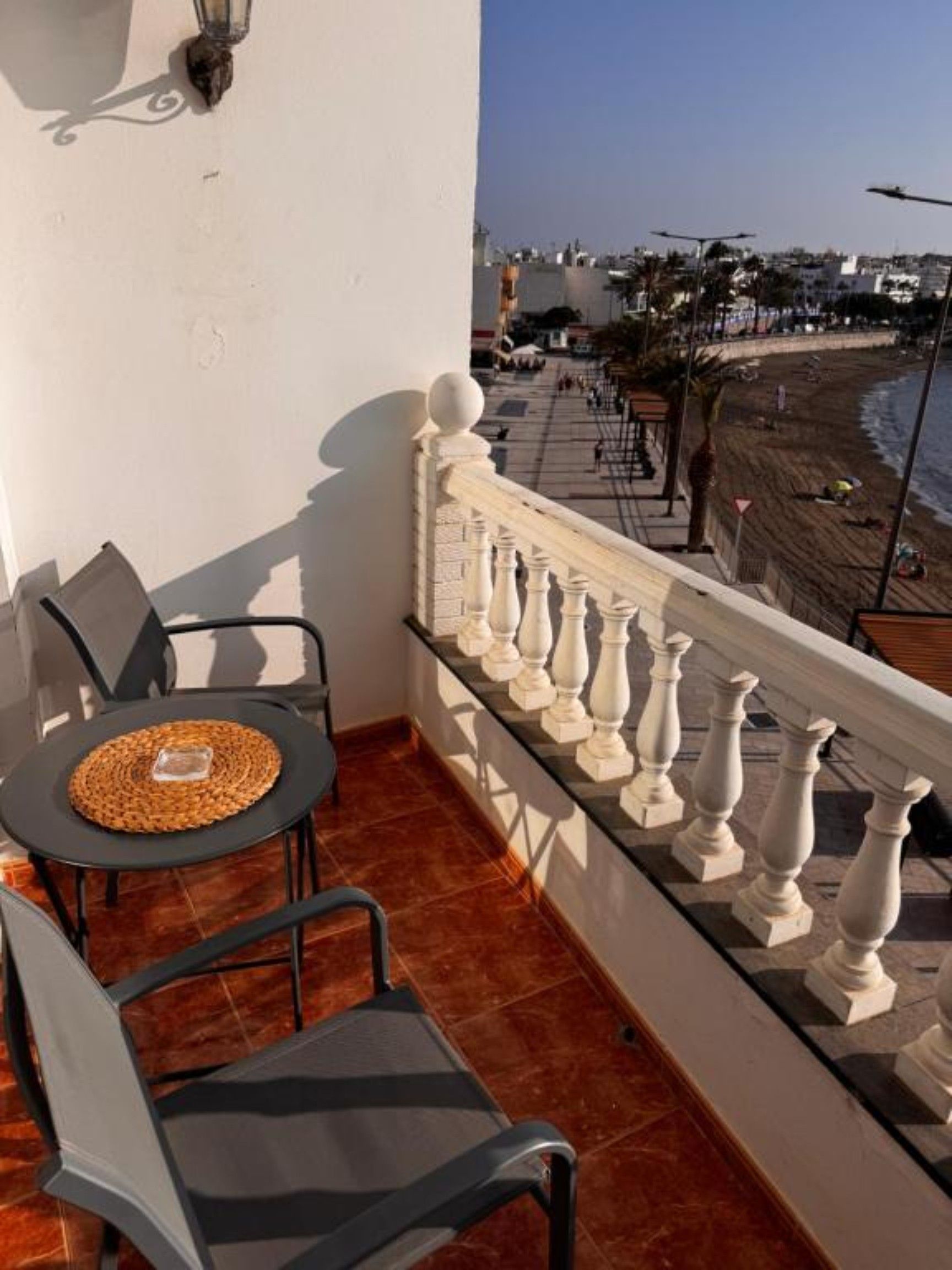 Un balcón con mesa y sillas, barandilla y vista a la playa y al paisaje urbano.