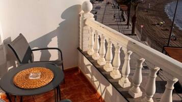 Un balcón con mesa y sillas, barandilla y vista a la playa y al paisaje urbano.