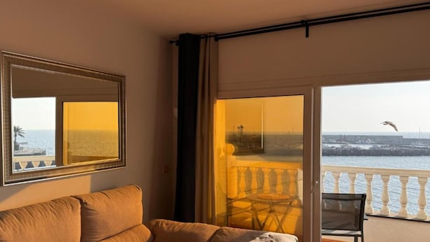 Una habitación con sofá, una silla, un balcón con barandilla y vistas al mar.
