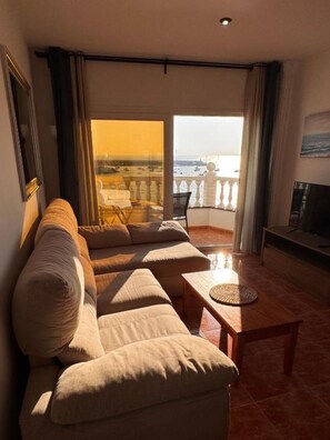 Een woonkamer met een bank, een salontafel en uitzicht op zee vanaf een balkon.