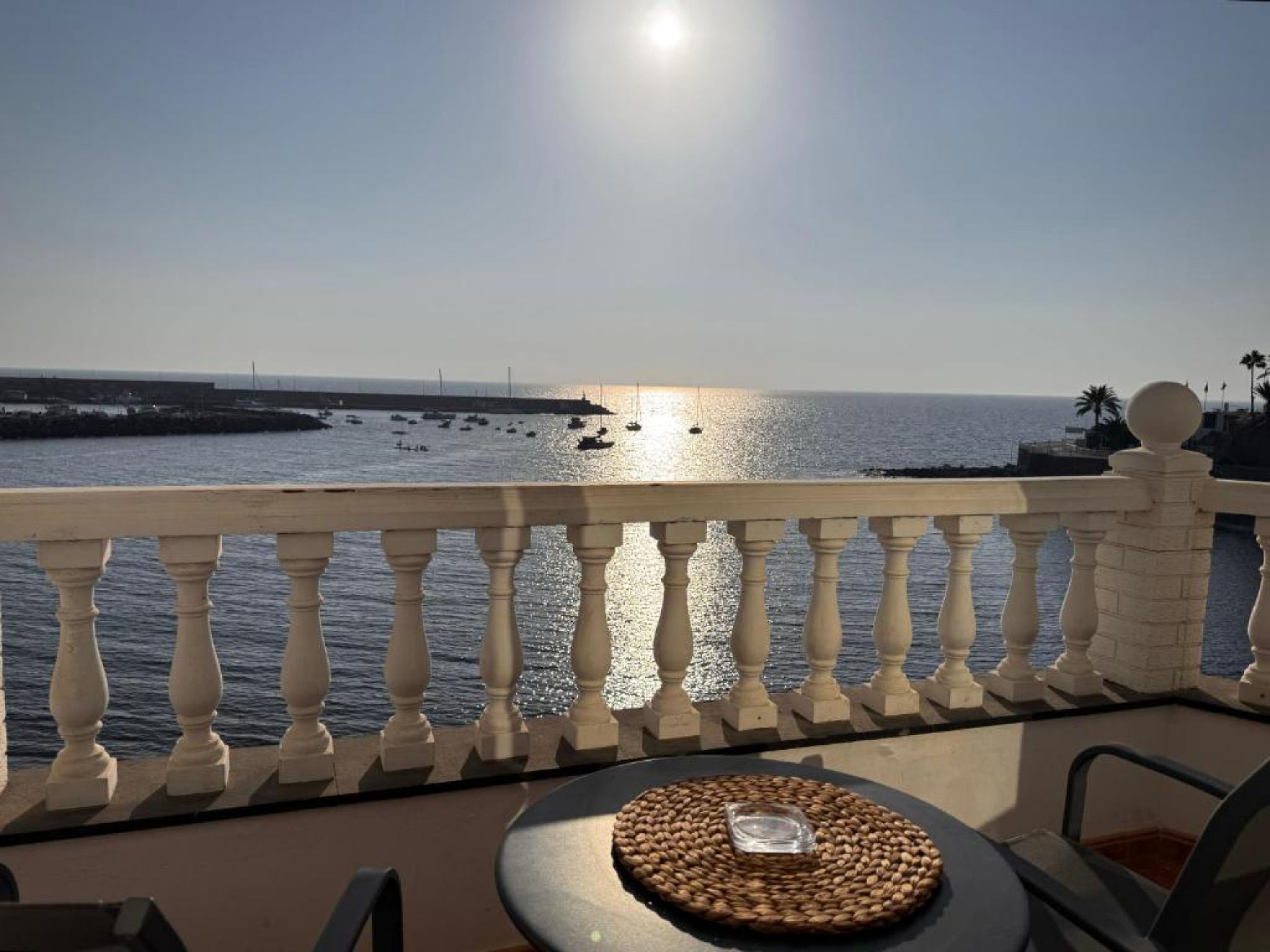 En balkon med udsigt over havet, et rundt vævet bord og en stol.