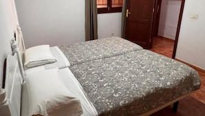 Una cama individual con una colcha estampada y almohadas blancas en una habitación con una puerta de madera y una ventana con cortinas.