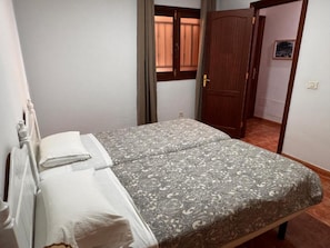 Een enkel bed met een beddengoed met een patroon en witte kussens in een kamer met een houten deur en een raam met gordijnen.