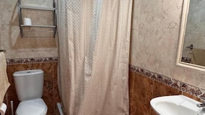 Un baño con cortina de ducha, inodoro, lavamanos y un espejo en la pared.