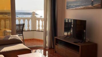 Una sala de estar con televisor, sofá, mesa de centro y balcón con vista al mar.