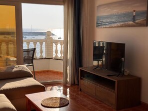 Una sala de estar con televisor, sofá, mesa de centro y balcón con vista al mar.