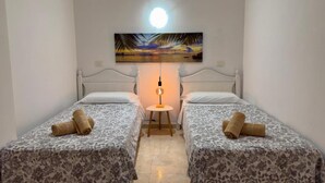 Una habitación con dos camas, cada una con una colcha estampada y una toalla enrollada. Una mesa con una lámpara se encuentra entre las camas.