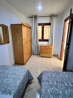 Een slaapkamer met twee bedden, een kledingkast, een dressoir en een raam met gordijnen.