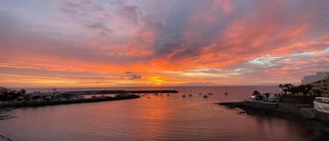 Atardecer costero con barcos, mar en calma y edificios a lo largo de la costa.