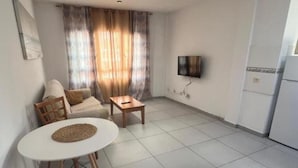 En kompakt, moderne lejlighed med spiseplads, sofa, fjernsyn ophængt på væggen og et tekøkken.