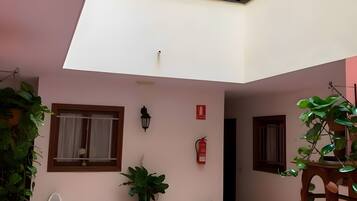 Un patio amplio con techo alto, una mesita, una planta en maceta y un extintor en la pared.