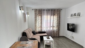 En moderne stue med sofa, spisebord og fjernsyn ophængt på væggen.