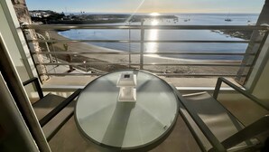 Un balcon avec une table en verre et une vue sur la plage et l’océan.