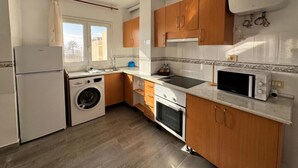 Une cuisine compacte équipée d’un lave-linge, d’un four, d’un four à micro-ondes et de meubles de rangement en bois.