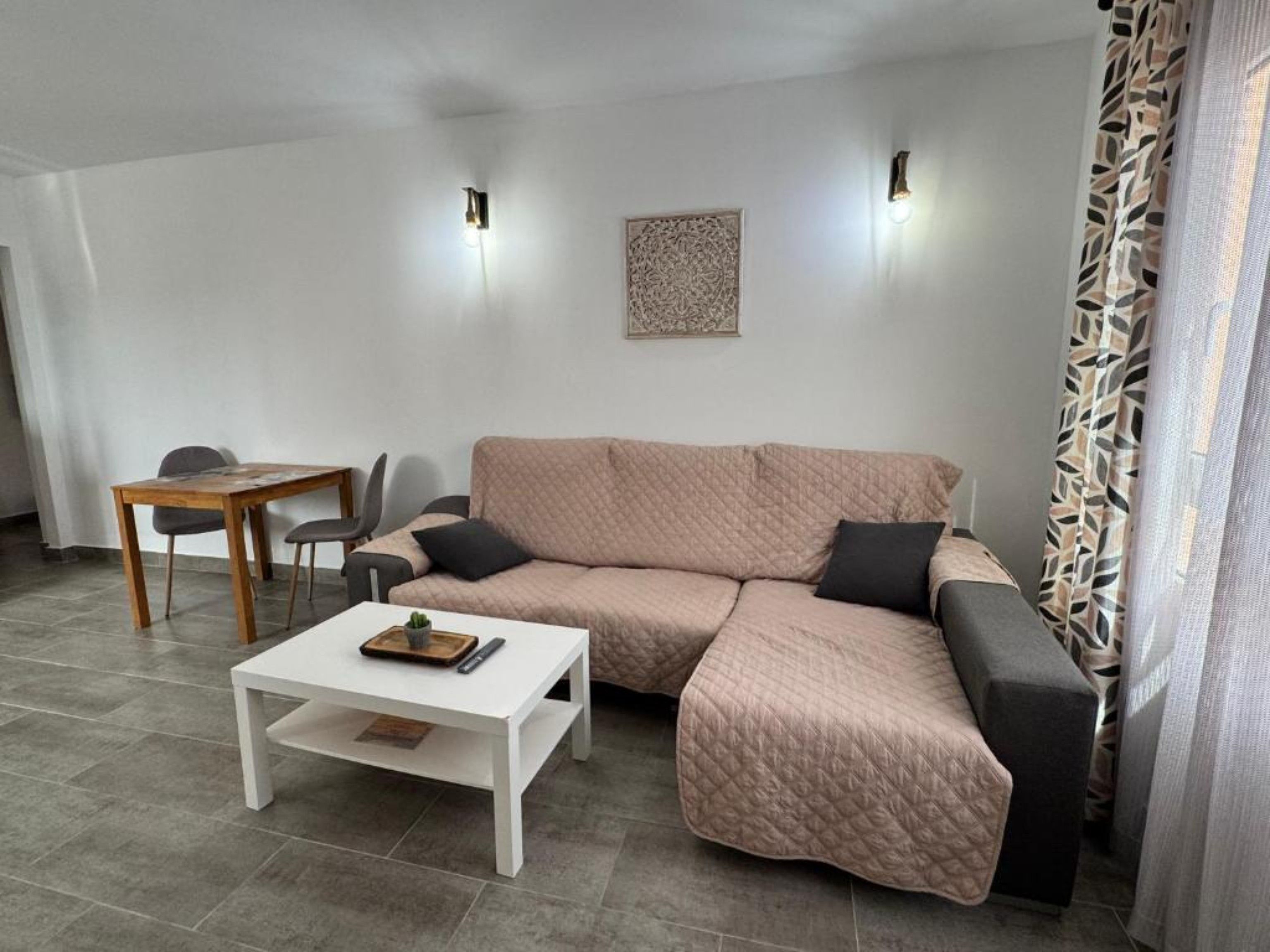 Een moderne woonkamer met een hoekbank, een witte salontafel en een eethoek met een houten tafel en stoelen.