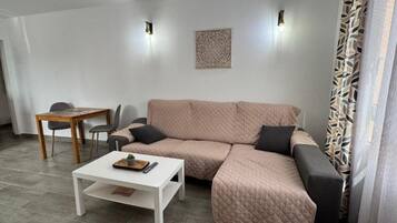 Een moderne woonkamer met een hoekbank, een witte salontafel en een eethoek met een houten tafel en stoelen.