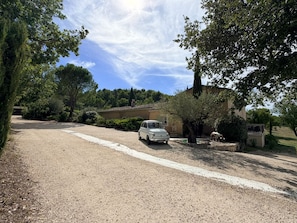 A gravel driveway leading to a white car parked in front of a house with a garden.