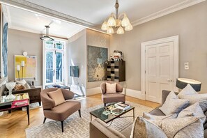 A spacious living room with a large window, a chandelier, and a door. - St John s Wood 4-bed House Huge Garden Grand Piano (London)