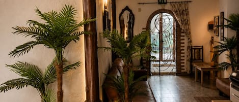 A hallway with a large wooden column, potted plants, a sofa, and a door with a wrought iron gate.