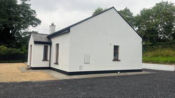 A white building with a black roof, a small porch, and a gravel driveway.