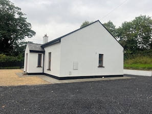 A white building with a black roof, a small porch, and a gravel driveway.