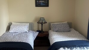 Un dormitorio con dos camas individuales, una mesita de noche con lámpara, un cuadro en la pared y una lámpara colgante.