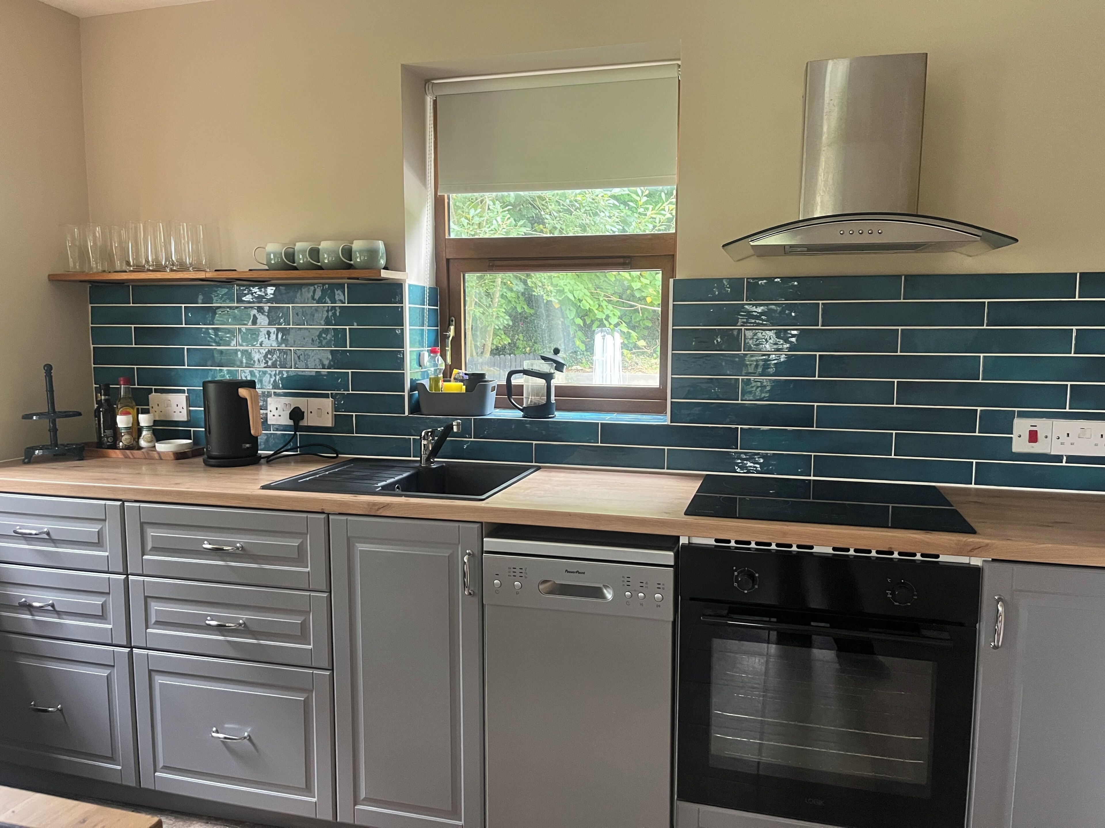 A modern kitchen with a dishwasher, oven, and a window with a view of greenery.