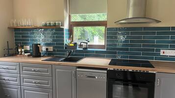 A modern kitchen with a dishwasher, oven, and a window with a view of greenery.