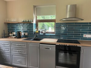 A modern kitchen with a dishwasher, oven, and a window with a view of greenery.