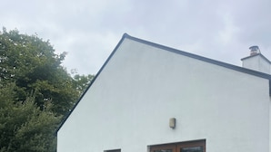 Un edificio blanco con puerta y ventanas marrones, un patio con mesa y sillas, y una zona verde al frente.