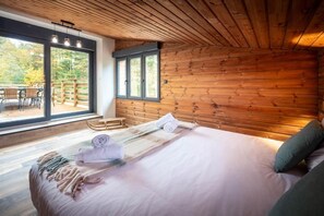 A bedroom with a large bed, a wooden ceiling, and a view of an outdoor deck. - La Perle Verte: A luxurious retreat with a pool, spa, and sauna (Gérardmer)
