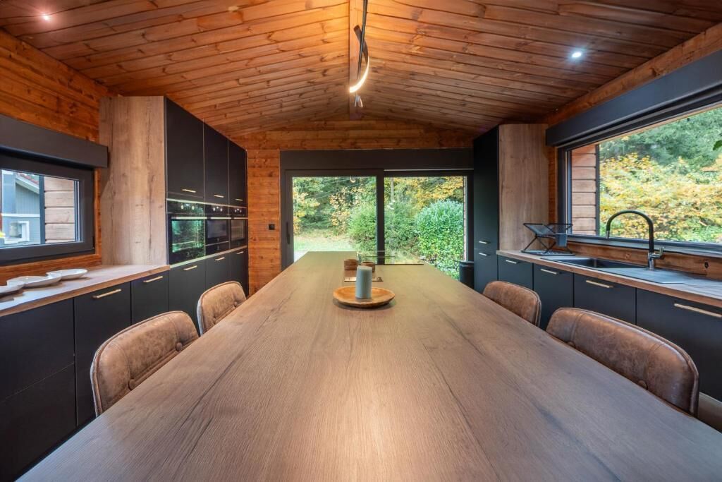 A modern kitchen with a wooden ceiling, large windows, and a central island.