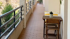 Een overdekt balkon met een betegelde vloer, een houten tafel met een stoel, en een plant in een pot.