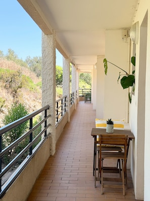 Ein überdachter Balkon mit gefliestem Boden, einem Holztisch, einem Stuhl und einem Blumentopf.