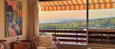 Una habitación con vistas a un paisaje montañoso, una silla de mimbre, una mesa con un cuenco y un cuadro en la pared.