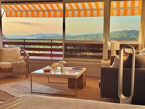 Ein Zimmer mit großem Fenster, einer Couch, einem Sessel, einem Couchtisch und einer Lampe.