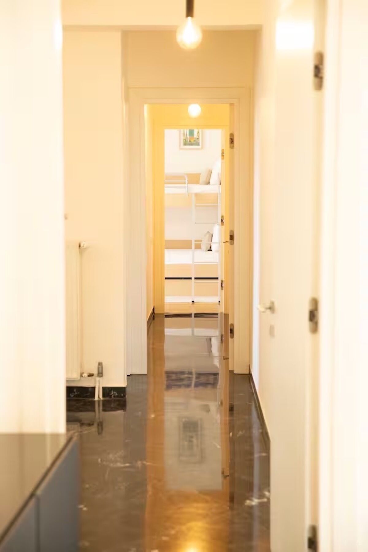 A hallway leading to a room with a bunk bed, a light fixture, and a door.
